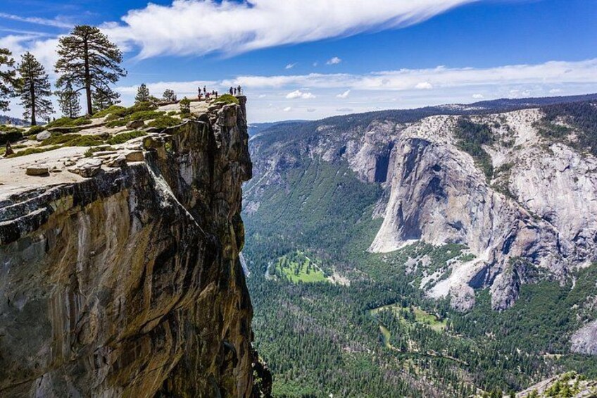 A cliff edge with a view of a valley and a prominent rock formation. 2