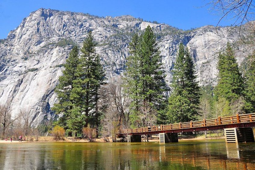 A wooden bridge over a calm lake with a rocky mountain in the background. 3