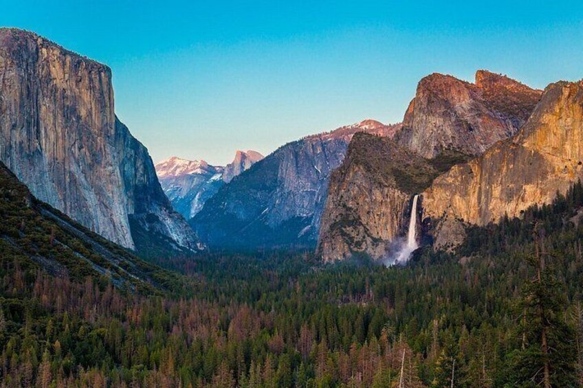 A waterfall in a canyon with towering cliffs and dense forest. 5