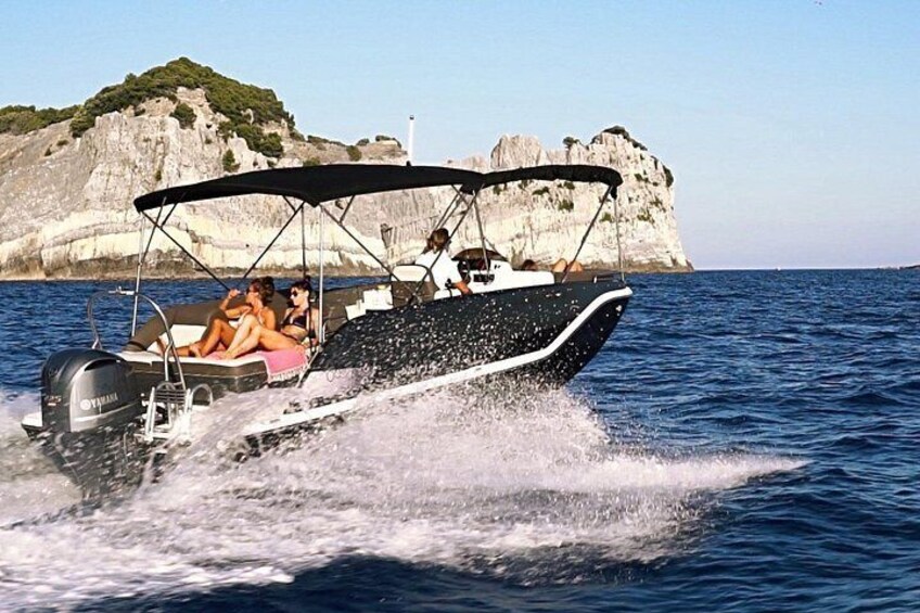 A motorboat with two people on board, moving through the water with a rocky coastline in the background. 3