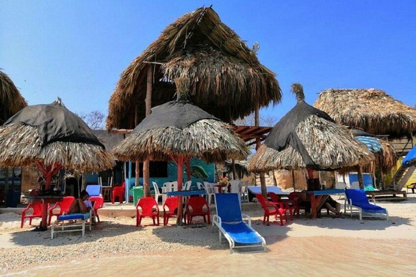 A beach with thatched umbrellas, lounge chairs, and a building in the background. 3