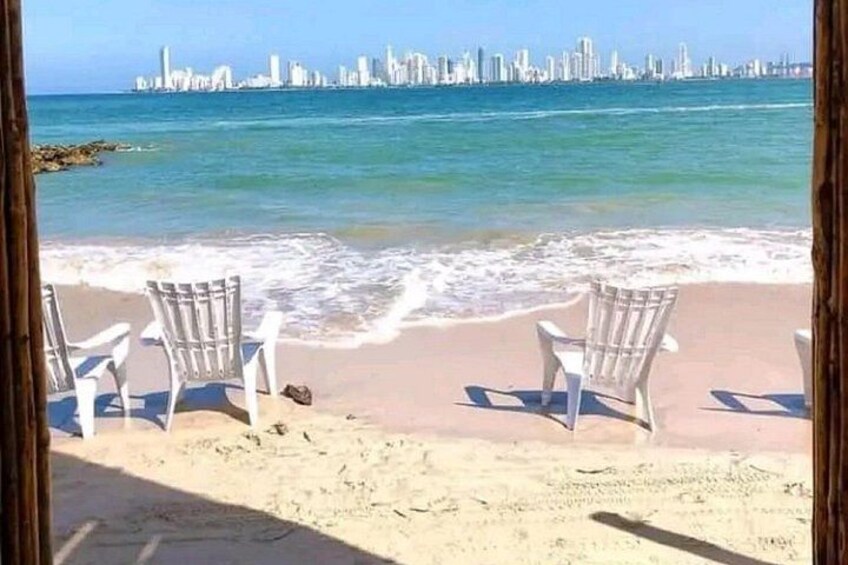 A beach with white chairs, a sandy shore, and a city skyline in the background. 1
