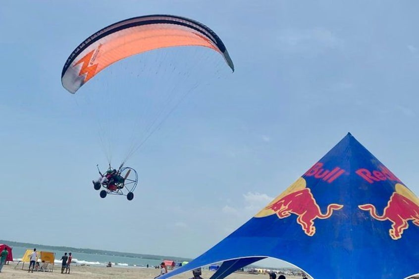 A paraglider flying over a beach with a Red Bull logo on a large kite. 1