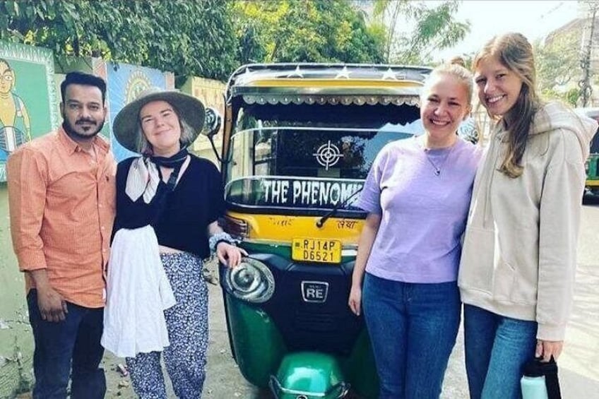 En grupp människor som poserar framför en automatisk rickshaw med ett registreringsnummer. 1