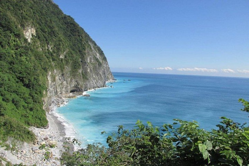 Un paysage côtier avec une plage, une mer bleue et limpide, et une falaise verdoyante. 4