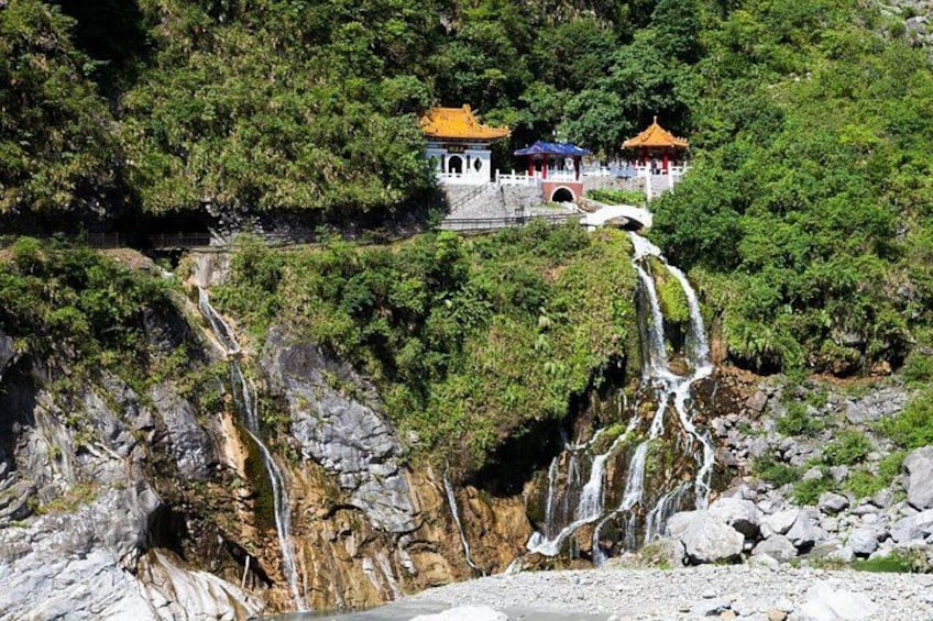 Une cascade se déversant le long d’une falaise rocheuse, entourée d’une végétation luxuriante et de bâtiments traditionnels aux toits colorés. 3