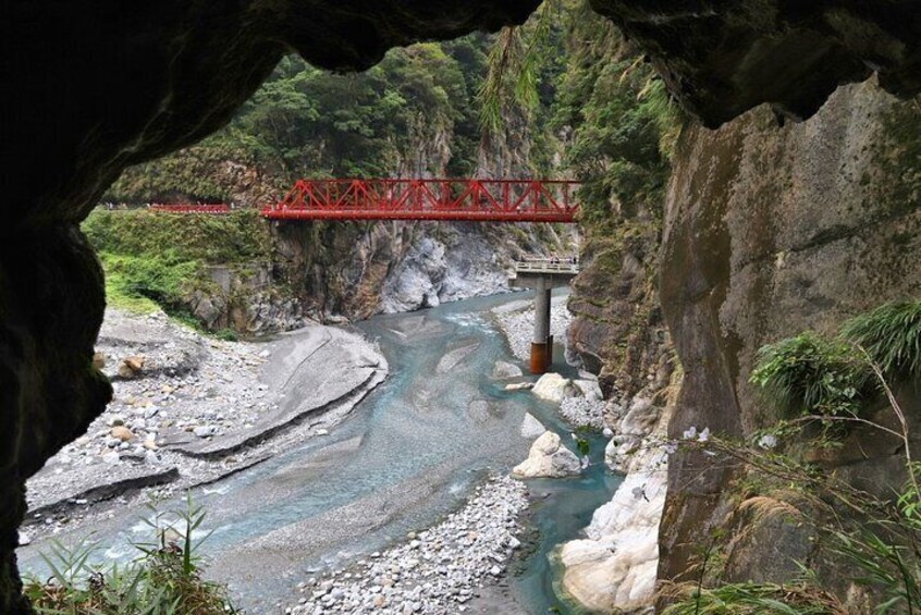 A river with a red bridge, rocky terrain, and greenery. 4