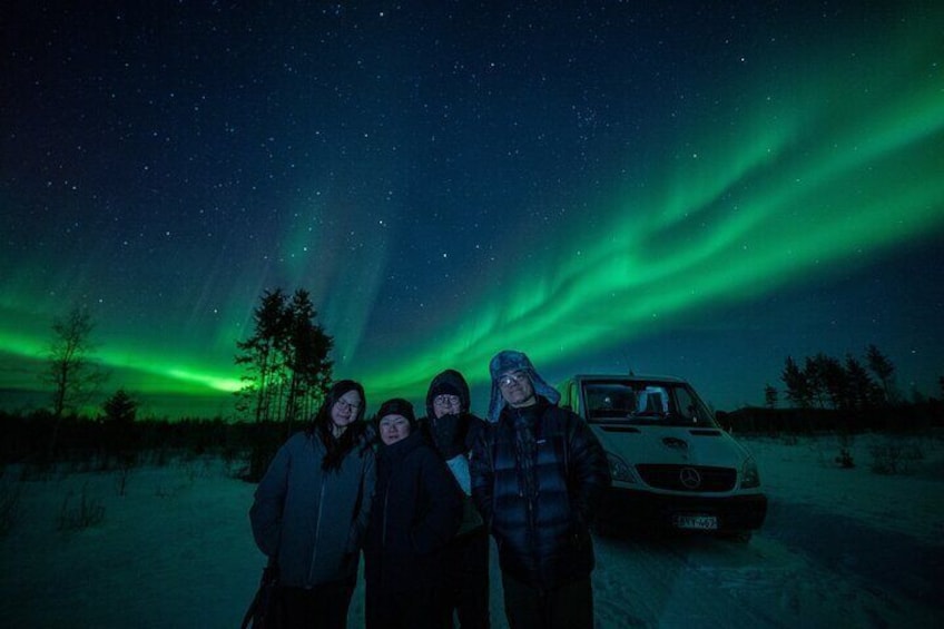 Three people standing in front of a car under a night sky with the Northern Lights. 1