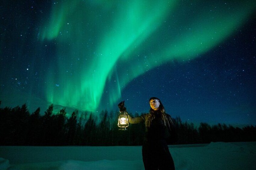A person standing on snow with a lantern, under a night sky with green aurora. 4
