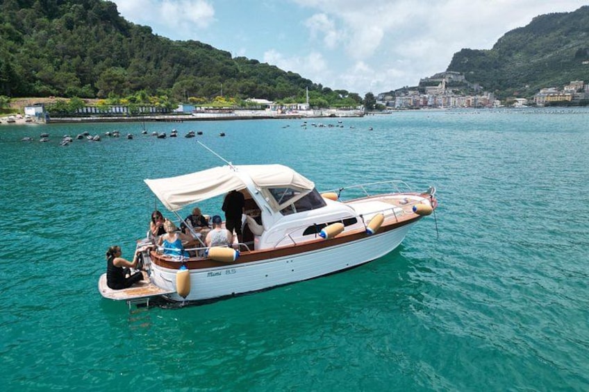 A white motorboat with a canopy, people on board, and a coastal town in the background. 1