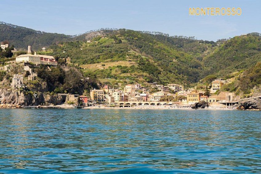 A coastal town with buildings on a hillside, a beach, and calm water. 3
