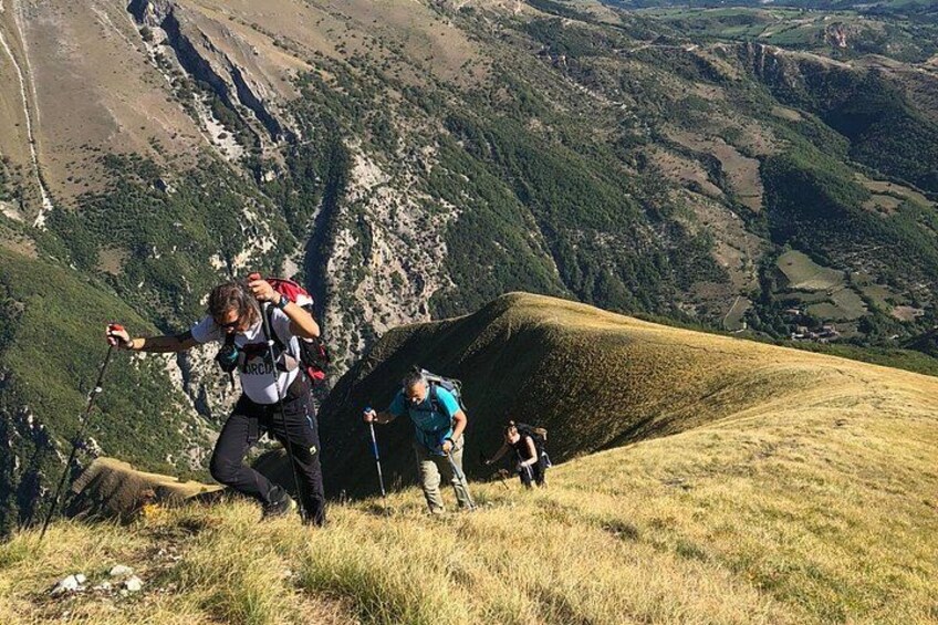 Un randonneur gravissant une colline herbeuse, avec un paysage montagneux en arrière-plan. 3