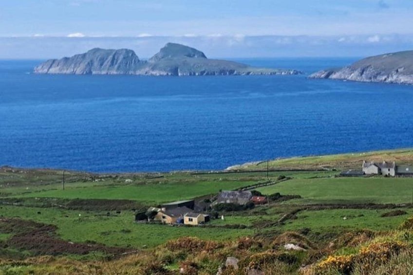 Un paisaje costero con un campo cubierto de hierba, una casa pequeña e islas rocosas a lo lejos. 2