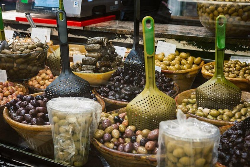 Diversas variedades de aceitunas en diferentes recipientes, como cuencos de madera y coladores de metal. 2