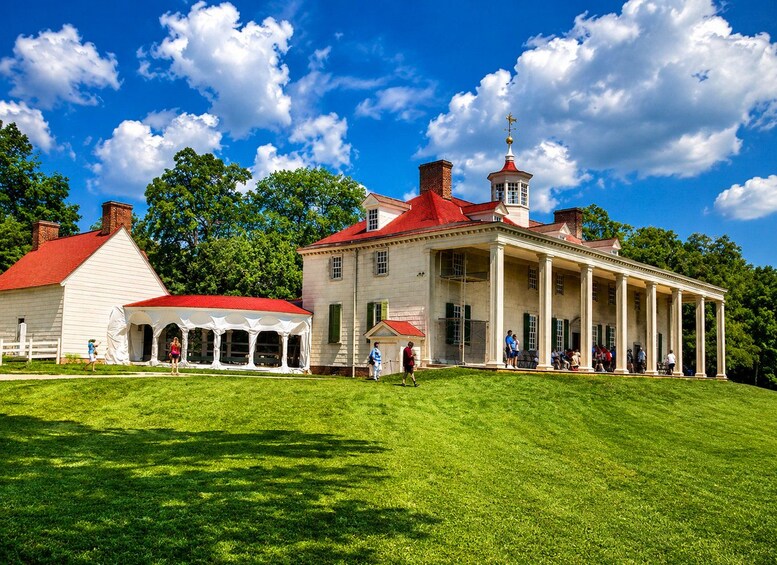 A historic building with a red roof and columns, surrounded by a well-maintained lawn and trees. 1