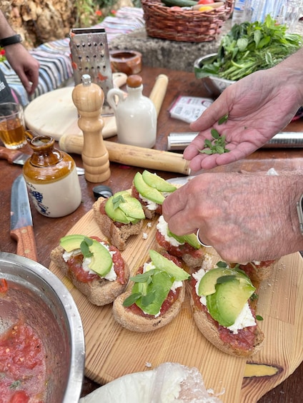 A person preparing bruschetta with tomatoes, cheese, and basil on a wooden board. 3