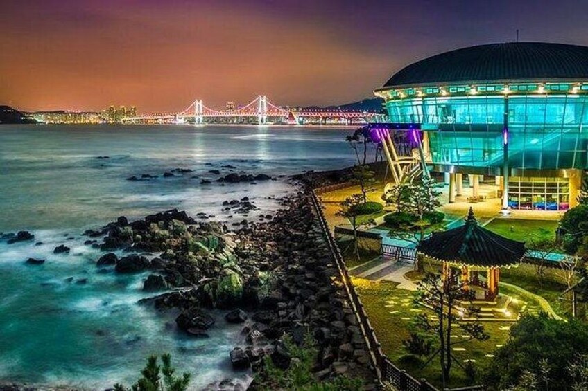 A coastal scene with a bridge, a building with illuminated windows, and a rocky shoreline. 3