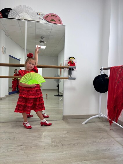 A child in a dance studio with a mirror, ballet barre, and a red fan. 2