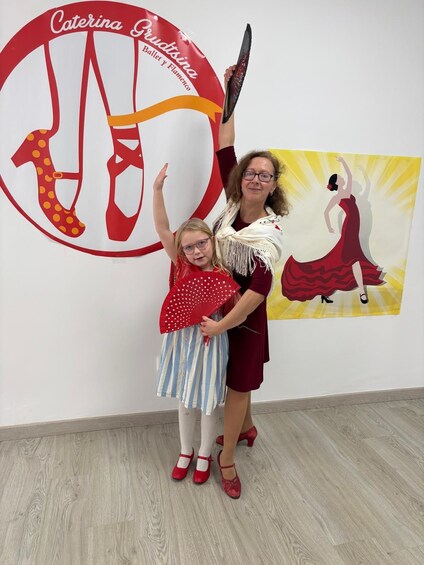 A woman and a child in a dance studio with a large poster of a dancer and the text 'Caterina Grudtizina Ballet y Flamenco'. 1