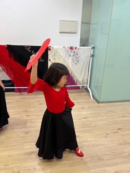 A person in a dance studio with a red fan, black skirt, and red shoes. 2