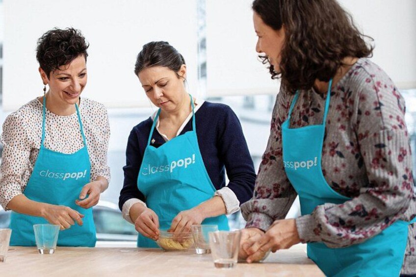 Three people wearing aprons with 'classpop!' text, preparing food at a table with glasses and a bowl. 4