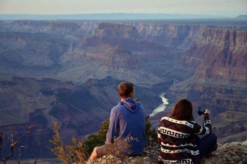 Two people sitting on a cliff overlooking a canyon with a river. 2