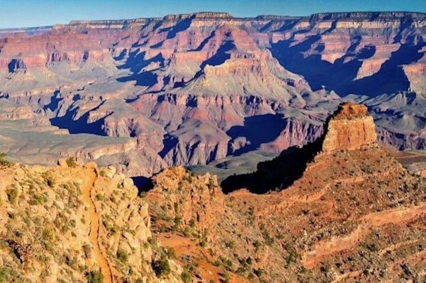 A vast canyon landscape with layered rock formations and a prominent rock spire. 3
