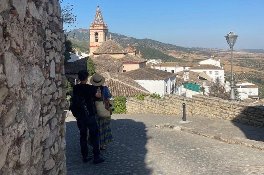 Un muro de piedra, una persona con una mochila, un edificio tradicional con un campanario y un farol. 2