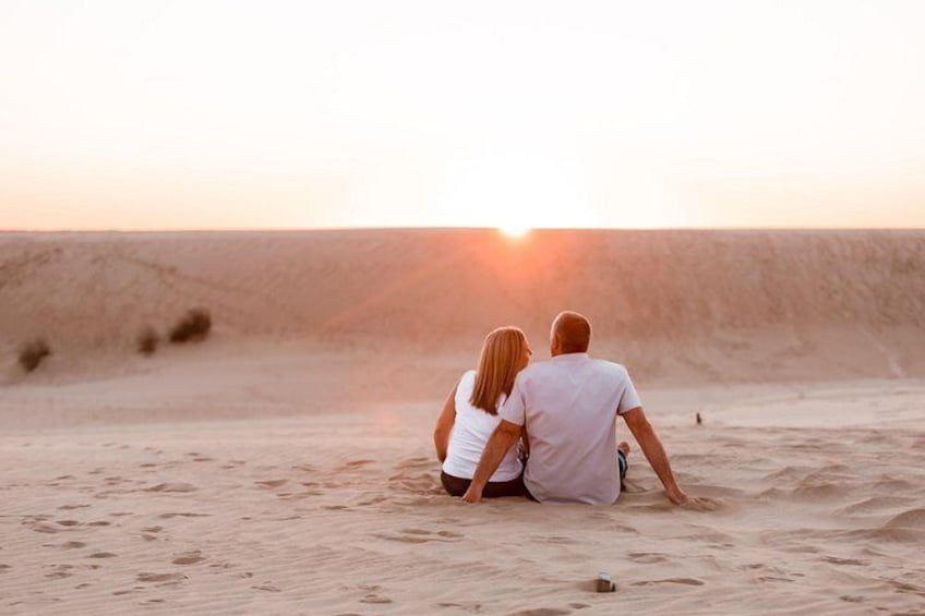 A couple sitting on a sandy beach facing a sunset. 3