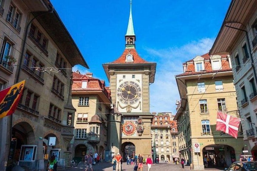 A historic square with a prominent clock tower, a church with a spire, and traditional European architecture. 4