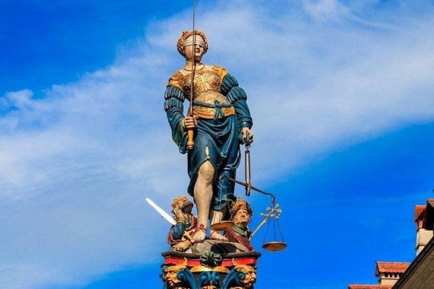 A statue of a figure holding a sword and a scale, standing on a decorated base with two smaller figures at its feet. 2