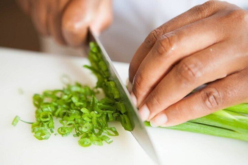 A person chopping green onions on a white cutting board. 2