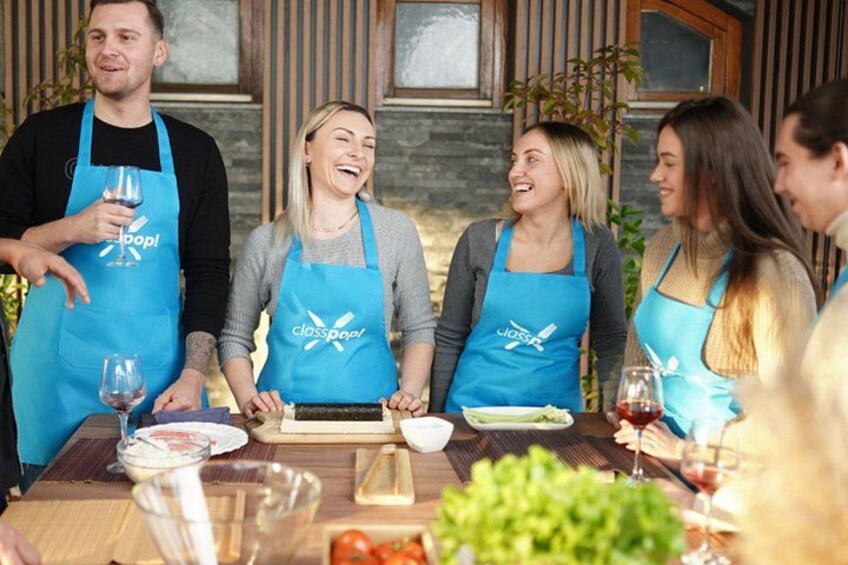 A group of people wearing blue aprons with the logo 'classpoo!' gathered around a wooden table with food and drinks. 2