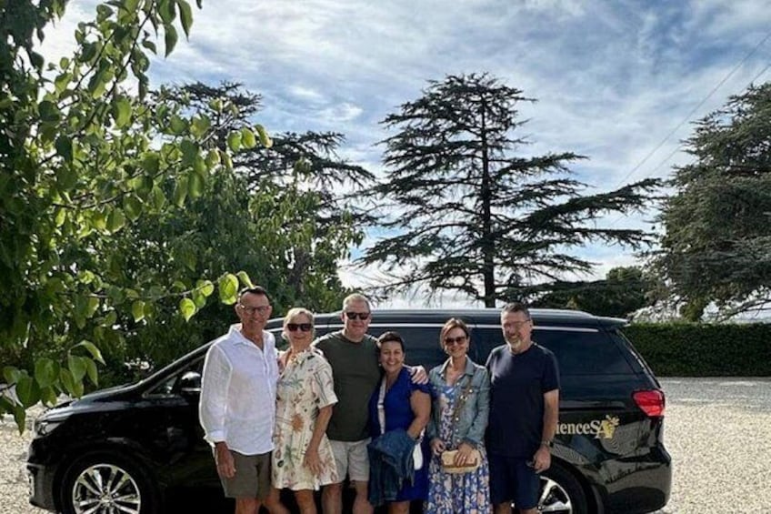 Eine Gruppe von Menschen steht vor einem schwarzen SUV, im Hintergrund ein Baum und ein klarer Himmel. 5