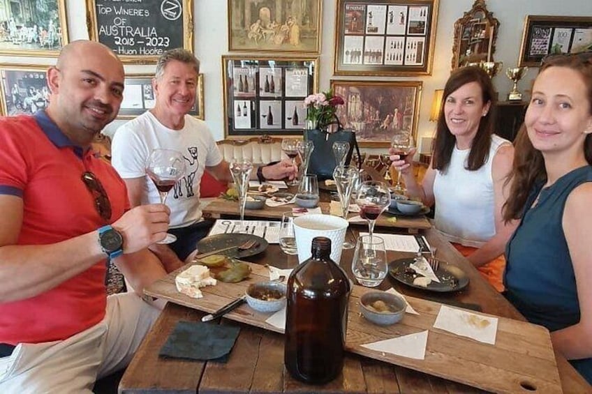 Eine Gruppe von Personen sitzt an einem Holztisch mit Weingläsern, Flaschen und Teller mit Essen. 1
