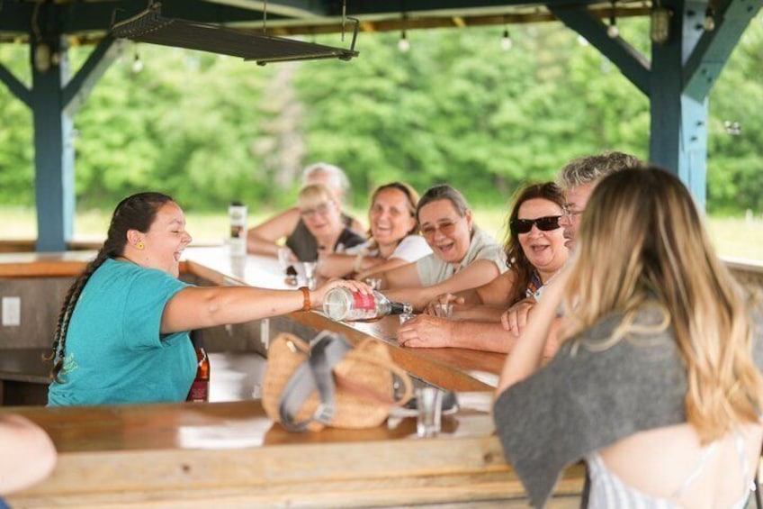 En grupp människor på en utomhuspicknick vid ett träbord och några träbänkar. 3