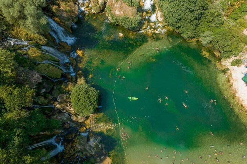 A clear aerial view of a lake surrounded by dense forest, with visible waterfalls and a boat anchored in the water. 3