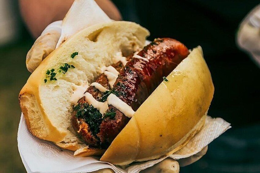 A hot dog with sausage, greens, and sauce in a bun. 1