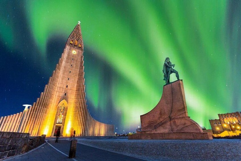 En kirke med spids tag og en statue på en sokkel under nordlys. 1