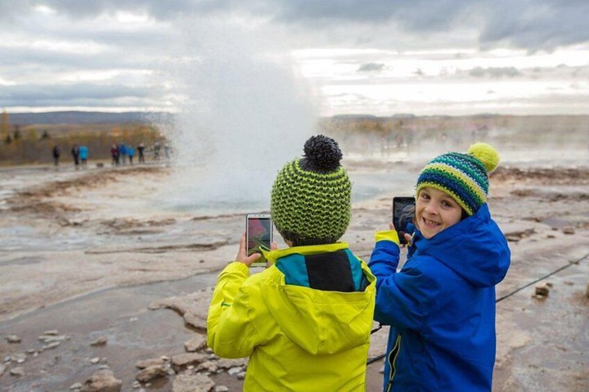 Two children taking photos of a geyser eruption. 2