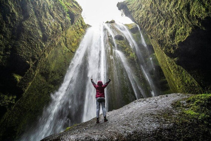A person standing on a rock with arms raised, facing a waterfall. 5
