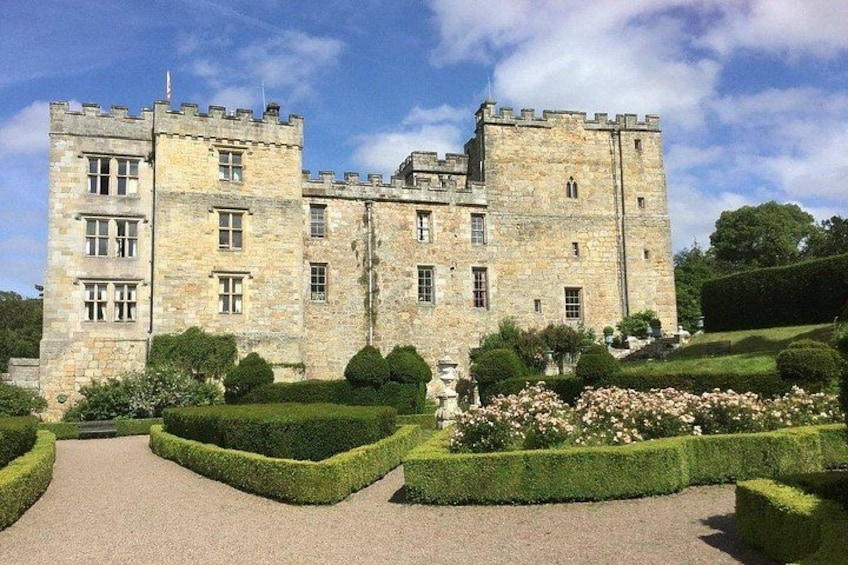 A castle with a symmetrical facade, a central tower, and a well-manicured garden with hedges and flower beds. 5