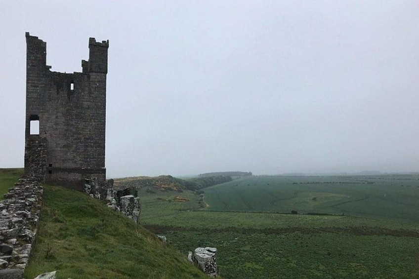 A ruined castle tower on a grassy hill with a valley in the background. 3