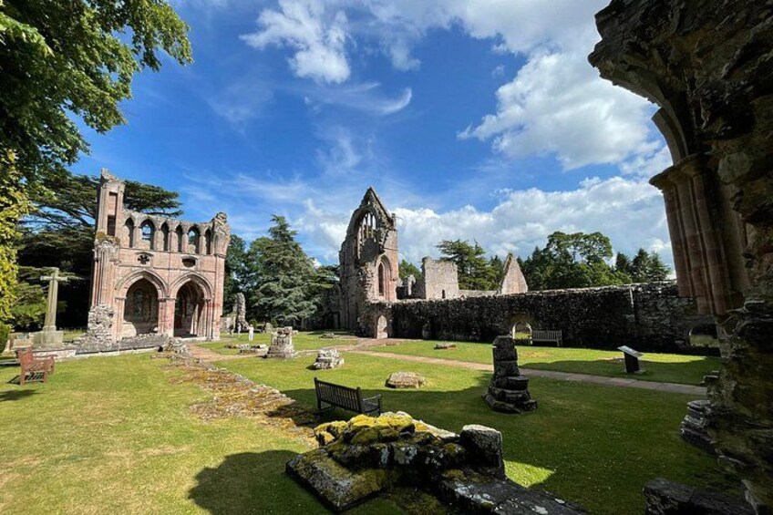 An ancient church ruin with a grassy courtyard, stone benches, and tombstones. 4