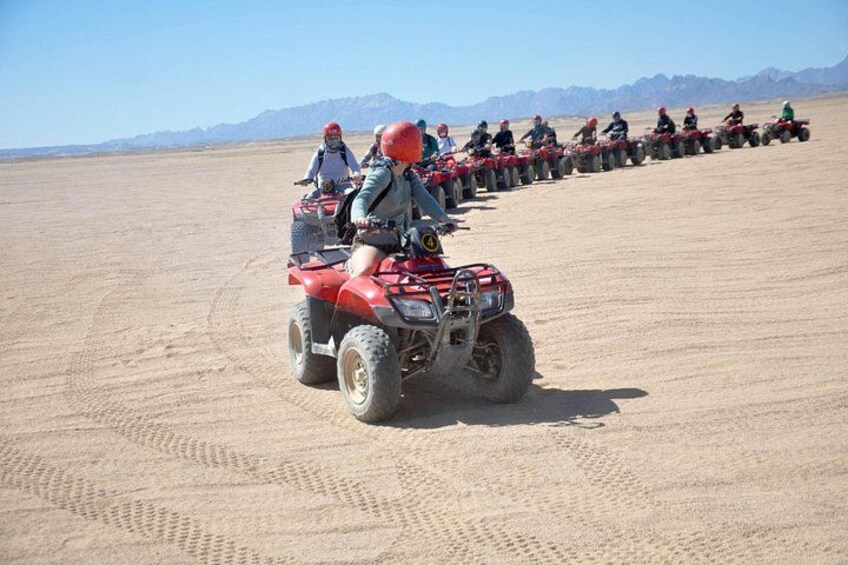 A group of people riding ATVs on a sandy terrain with mountains in the background. 4