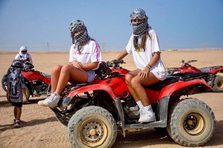 Two people on a red quad bike in a desert with a clear sky. 3