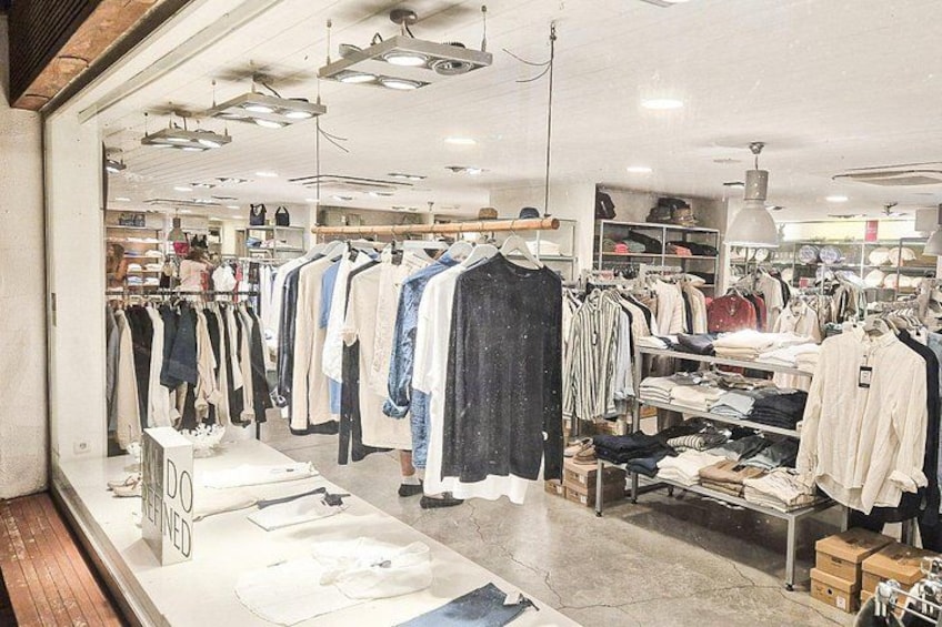 Een kledingwinkel met rekken vol kleding, tafels met opgevouwen artikelen en planken met schoenen. 2