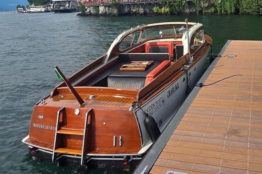 Een houten boot afgemeerd aan een steiger, met een hutje en zitgedeelte. 2