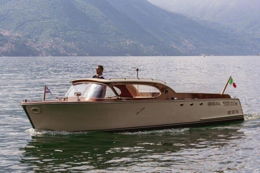 A vintage wooden boat with a flag, moving on calm water with mountains in the background. 5