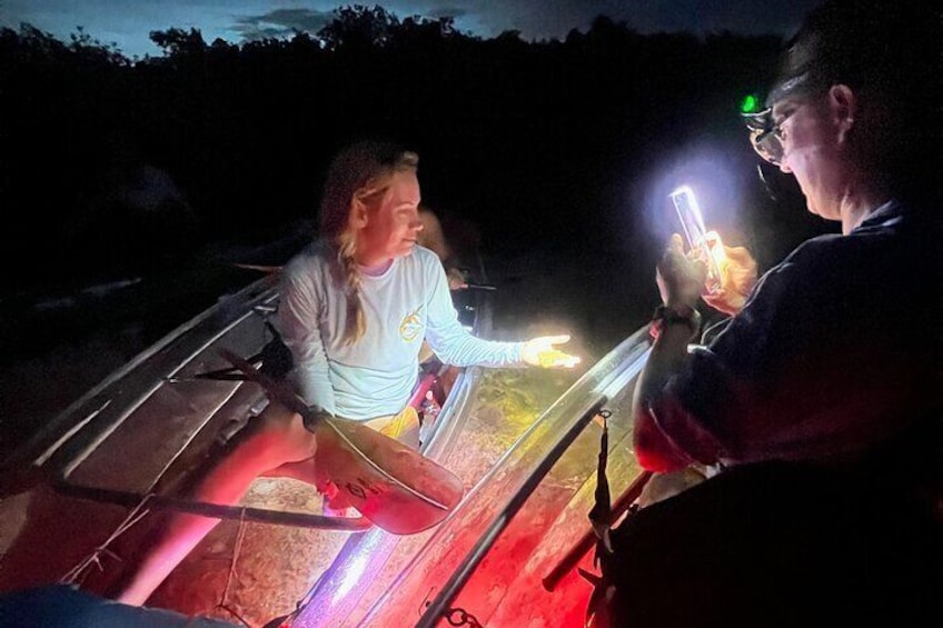 A person in a kayak on a river at night, illuminated by a flashlight. 2